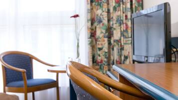 A wooden dining table with a television on it, a blue upholstered chair, and floral curtains in the background.