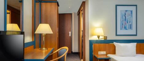 Une chambre d’hôtel comprenant un lit, un bureau avec une chaise, une télévision et deux lampes.