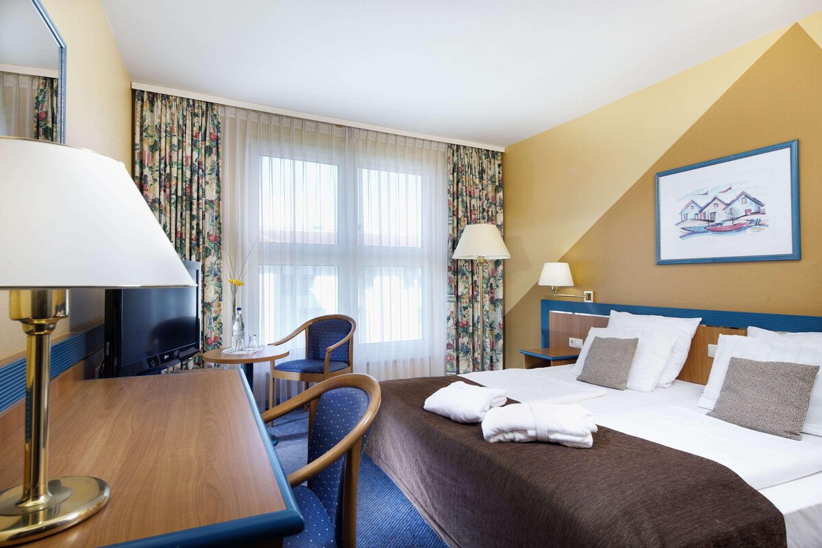 A hotel room with a bed, a desk, a chair, a television, and a window with curtains.