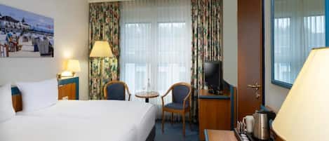 A hotel room with a bed, a desk, a chair, a television, and a window with curtains.