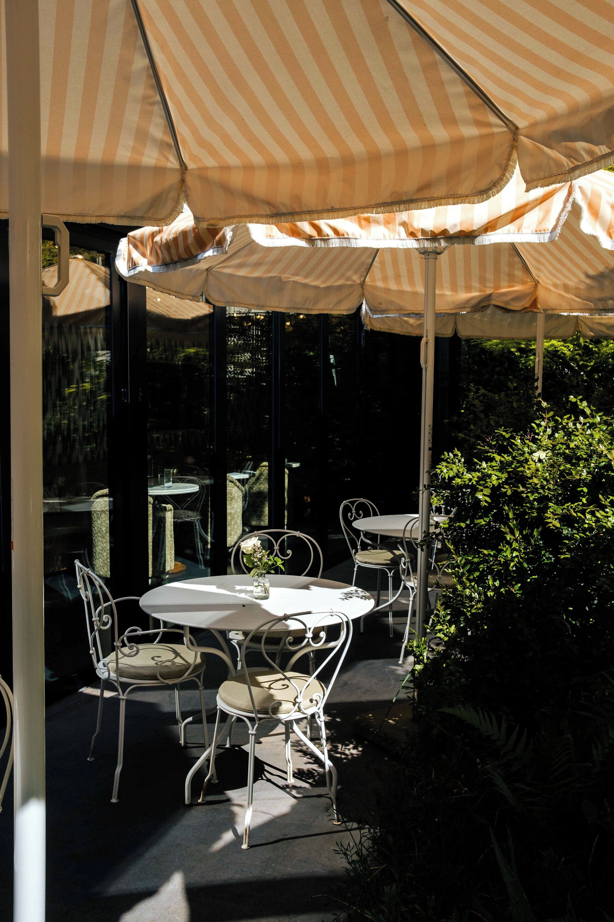 A covered outdoor seating area with striped canopies, metal chairs, and tables.