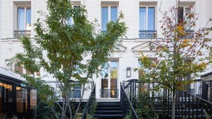 A building with a staircase leading to the entrance, surrounded by greenery and a fence. - Le 5 Particulier (Neuilly-sur-Seine)