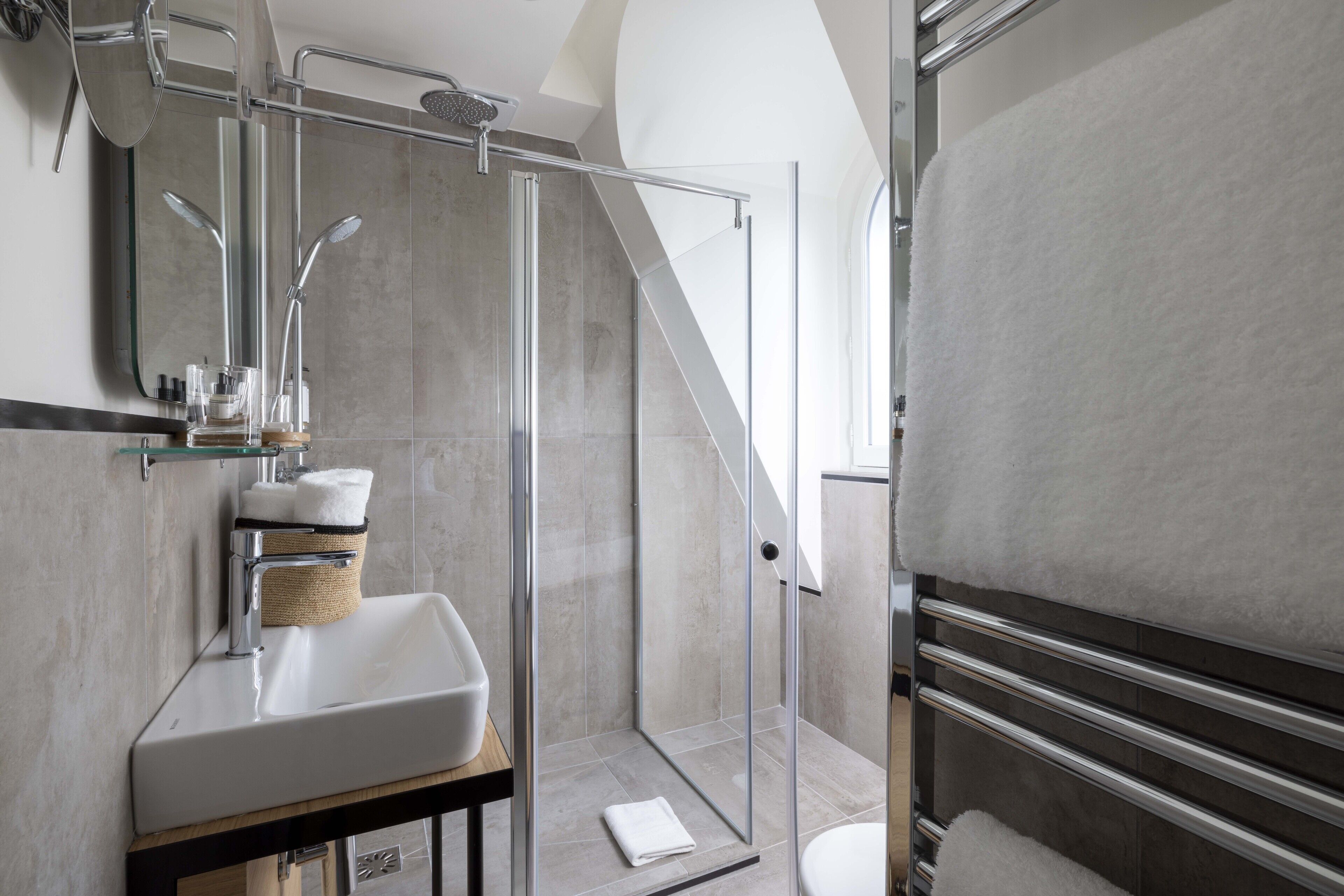 Un baño moderno con ducha envuelta en vidrio, un lavamanos blanco y un perchero para toallas.