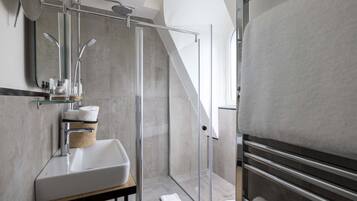 Un baño moderno con ducha envuelta en vidrio, un lavamanos blanco y un perchero para toallas.
