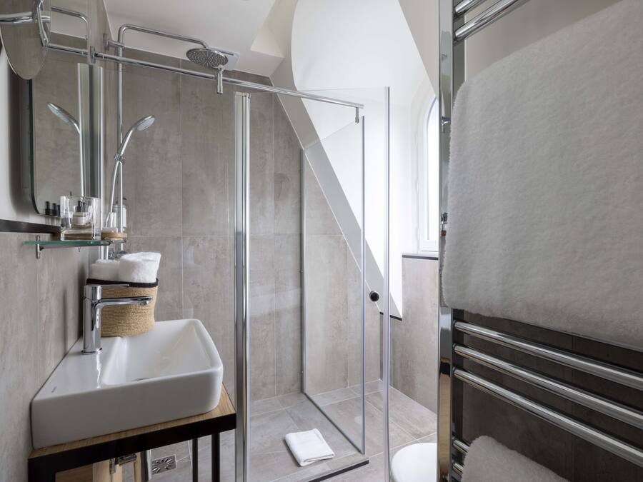Un baño moderno con ducha envuelta en vidrio, un lavamanos blanco y un perchero para toallas.