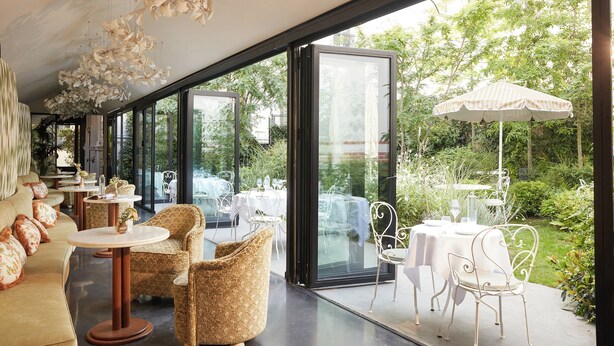 An indoor-outdoor dining area with glass walls, wicker furniture, and white metal chairs. - Le 5 Particulier (Neuilly-sur-Seine)