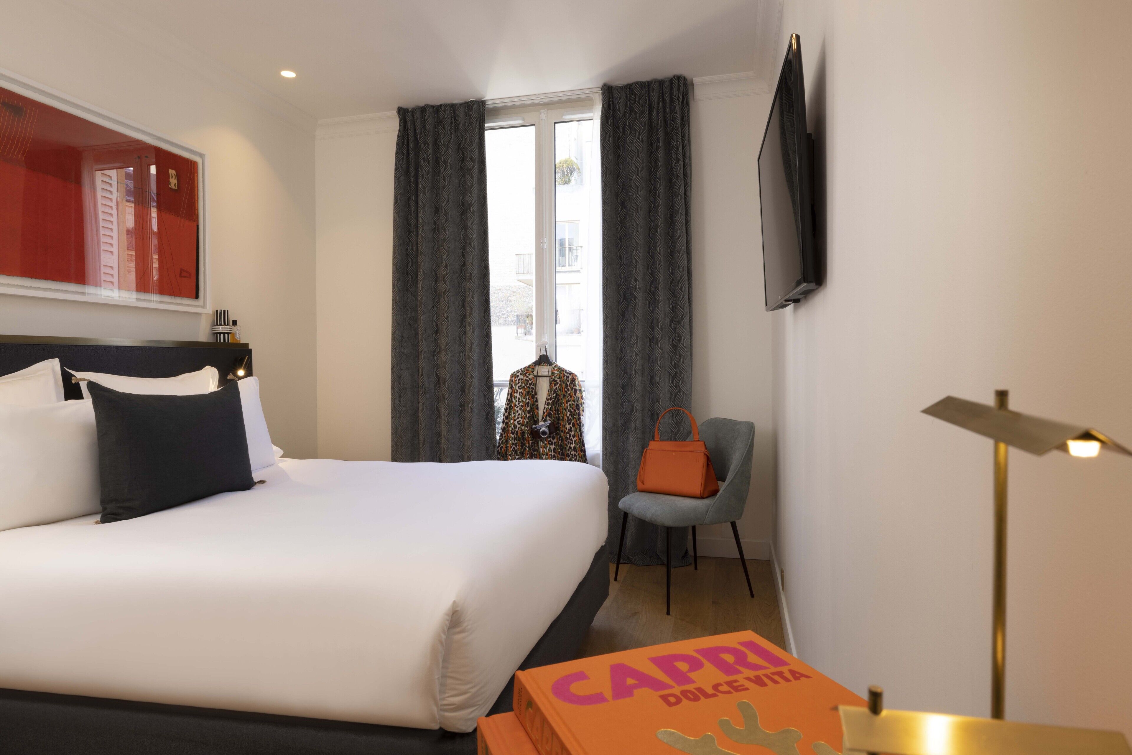 A hotel room with a large bed, a chair, a desk, a television, and a window with curtains.