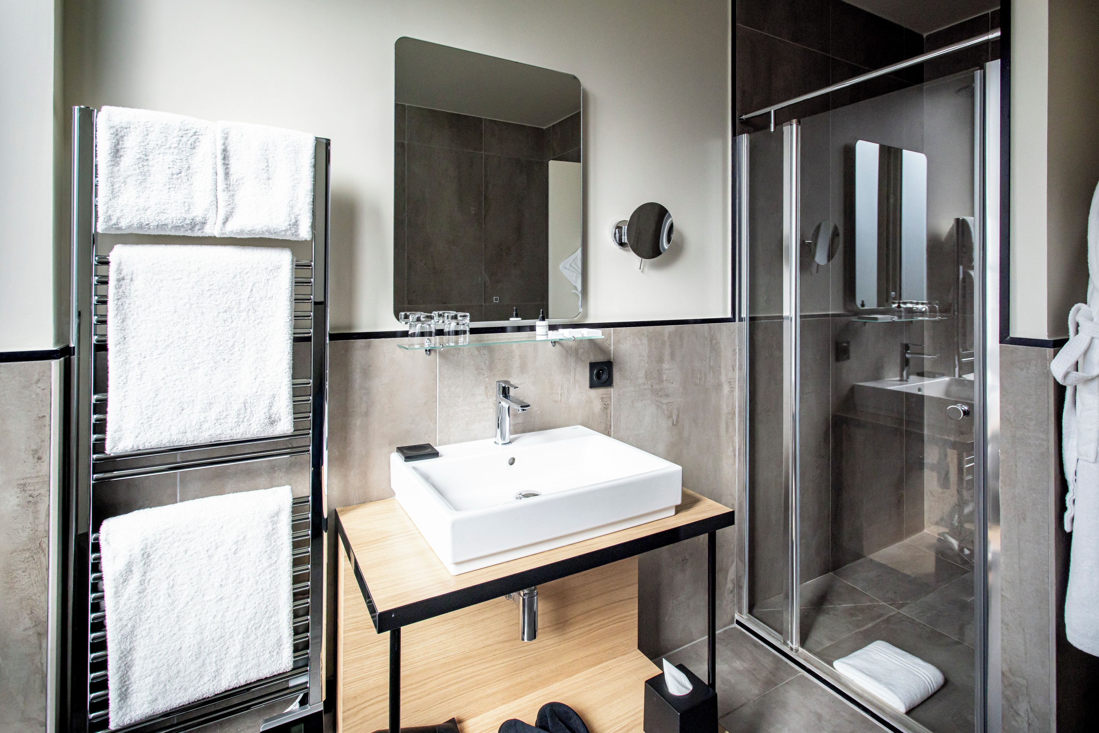 A modern bathroom with a glass shower enclosure, a white sink, and a towel rack with multiple towels.