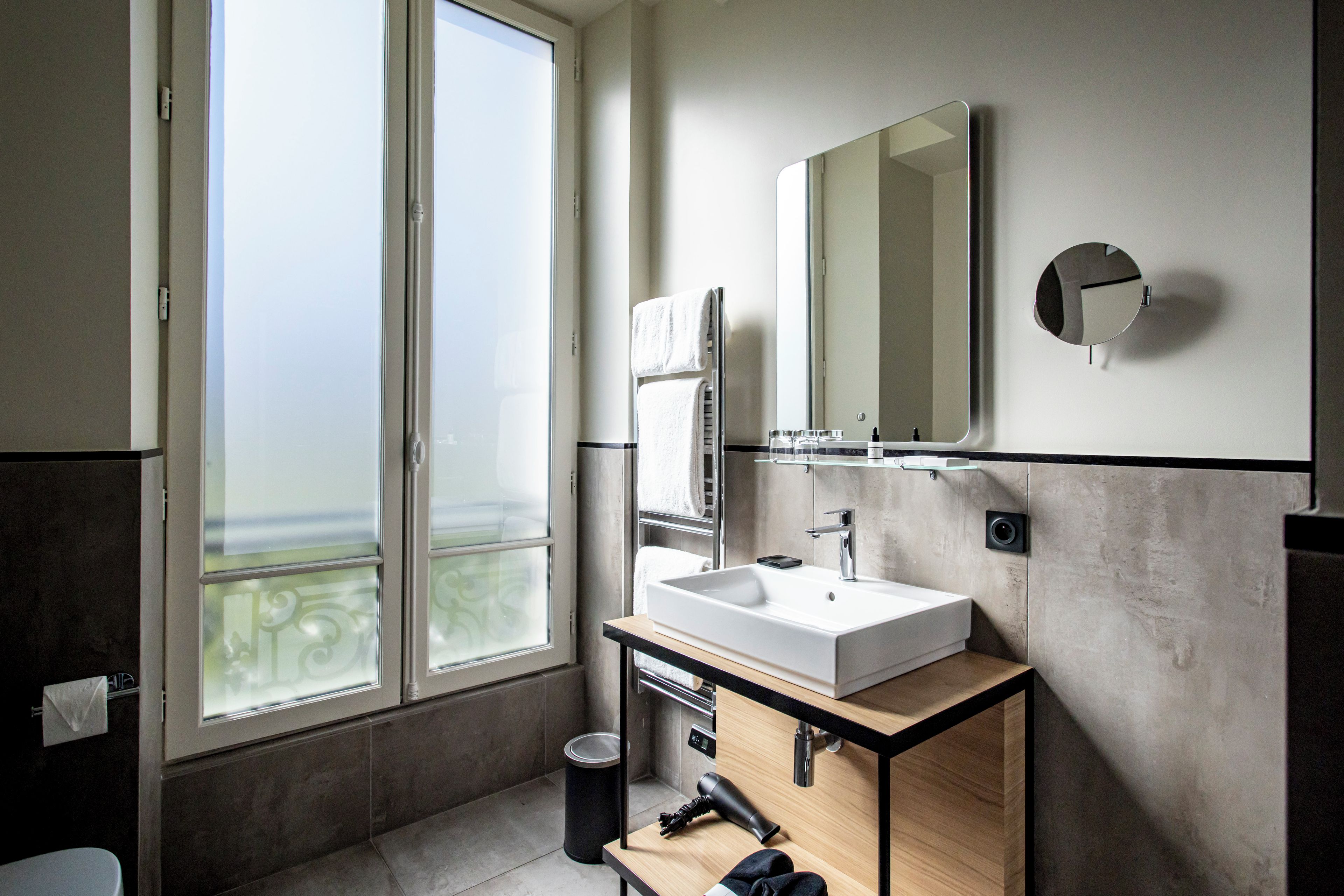 A modern bathroom with a large window, a white sink, a mirror, and a towel rack.