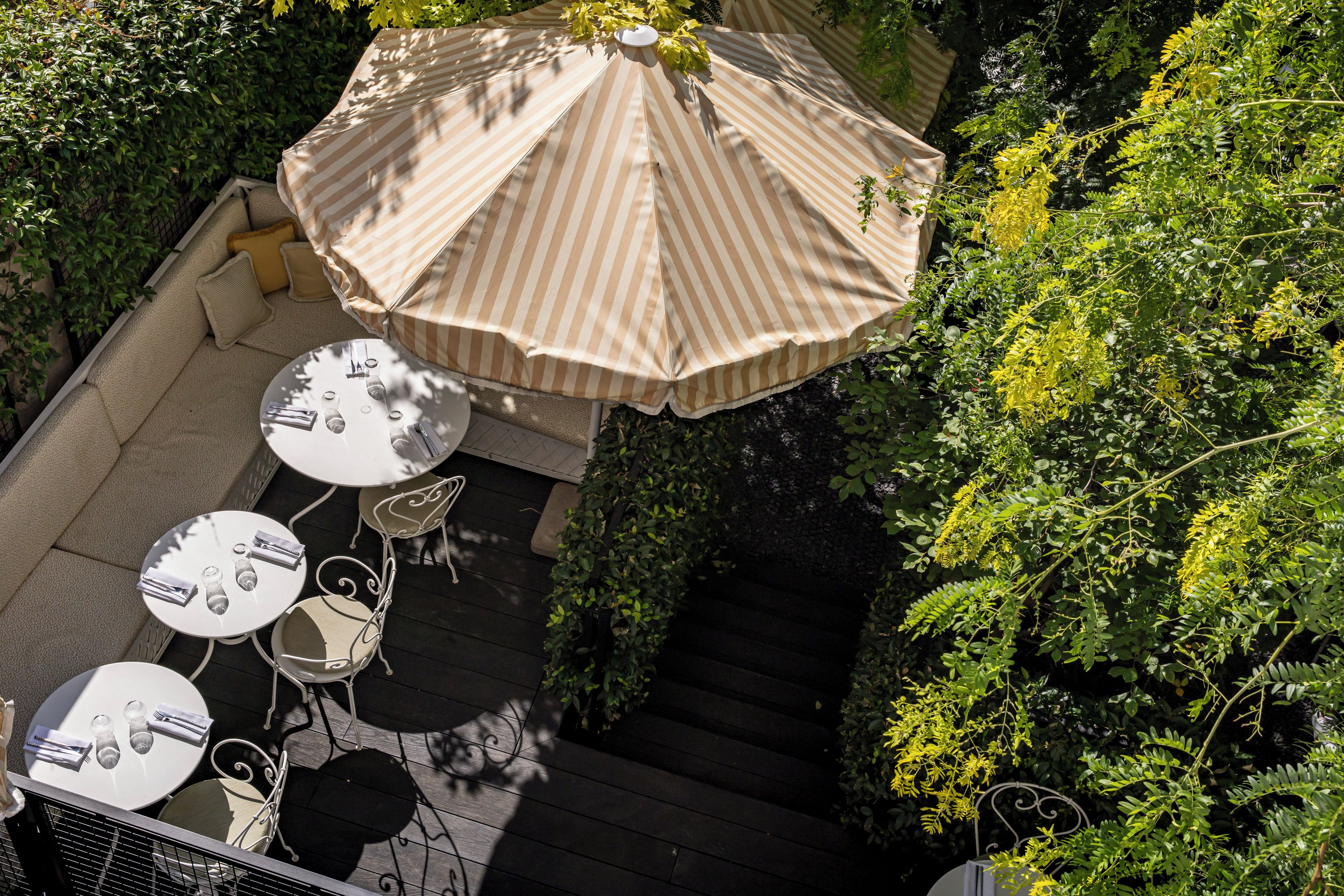 An outdoor seating area with tables and chairs, a striped umbrella, and lush greenery.