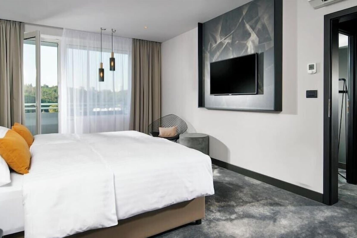 Habitación de hotel moderna con una cama grande, un televisor montado en la pared y vistas al exterior.