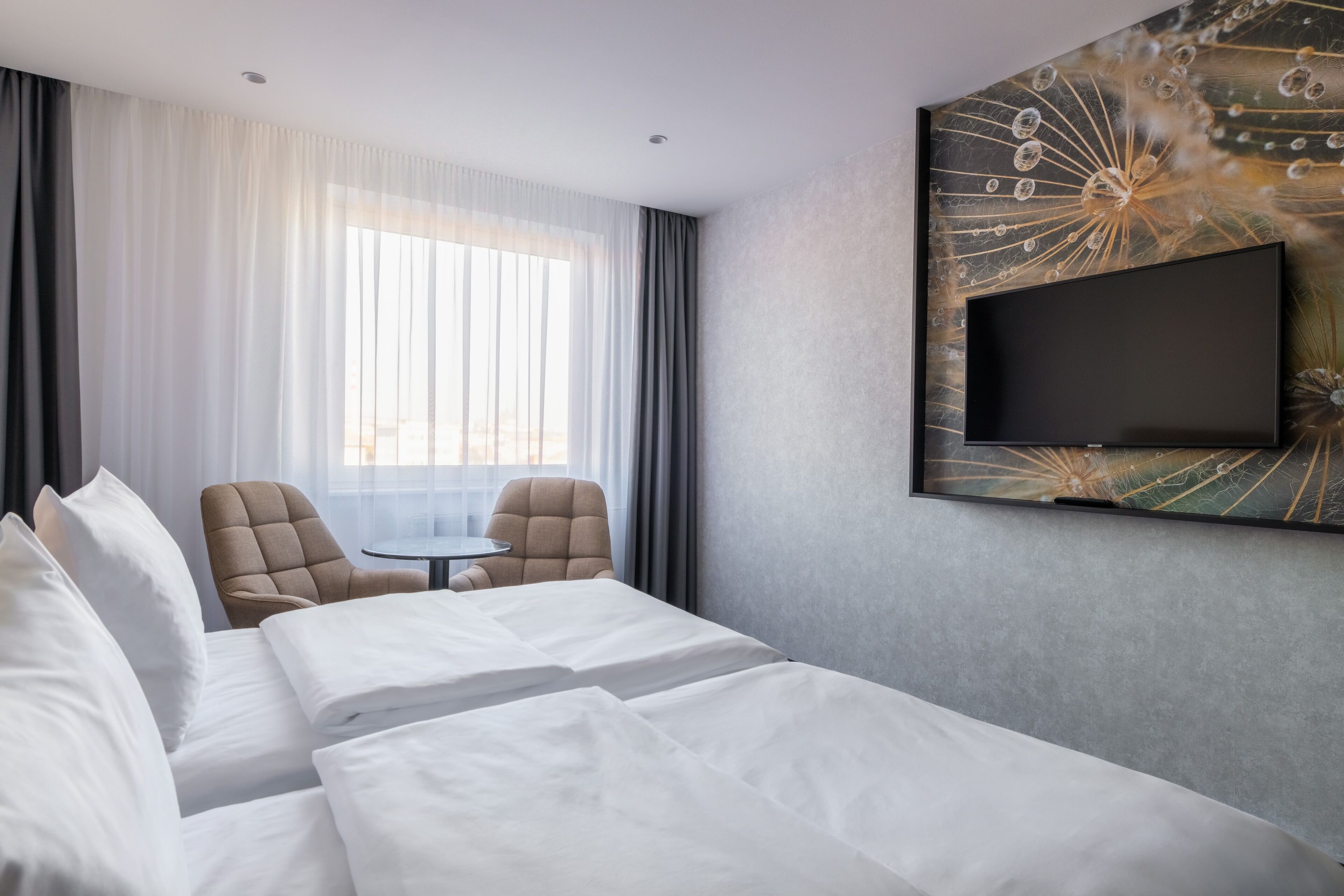 A hotel room with a large bed, two armchairs, a small table, and a TV mounted on the wall.