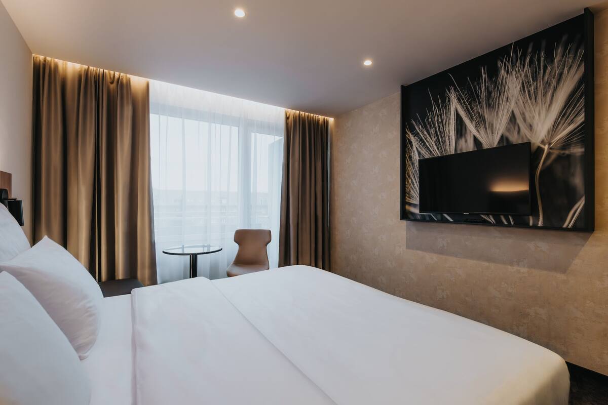 A hotel room with a large bed, a small round table, and a TV mounted on the wall.