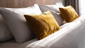 A bed with white bedding and two mustard-colored pillows, a wooden headboard, and a window with curtains. - Orea Congress hotel Brno (Brno)