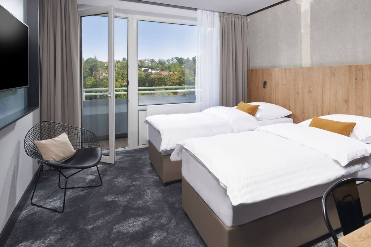 A hotel room with two beds, a chair, a desk, and a large window with a view.