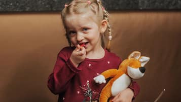 A child sitting at a table with a stuffed toy, a cup, and a small jar.