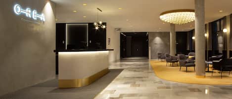 A modern hotel lobby with a reception desk, seating area, and a chandelier.