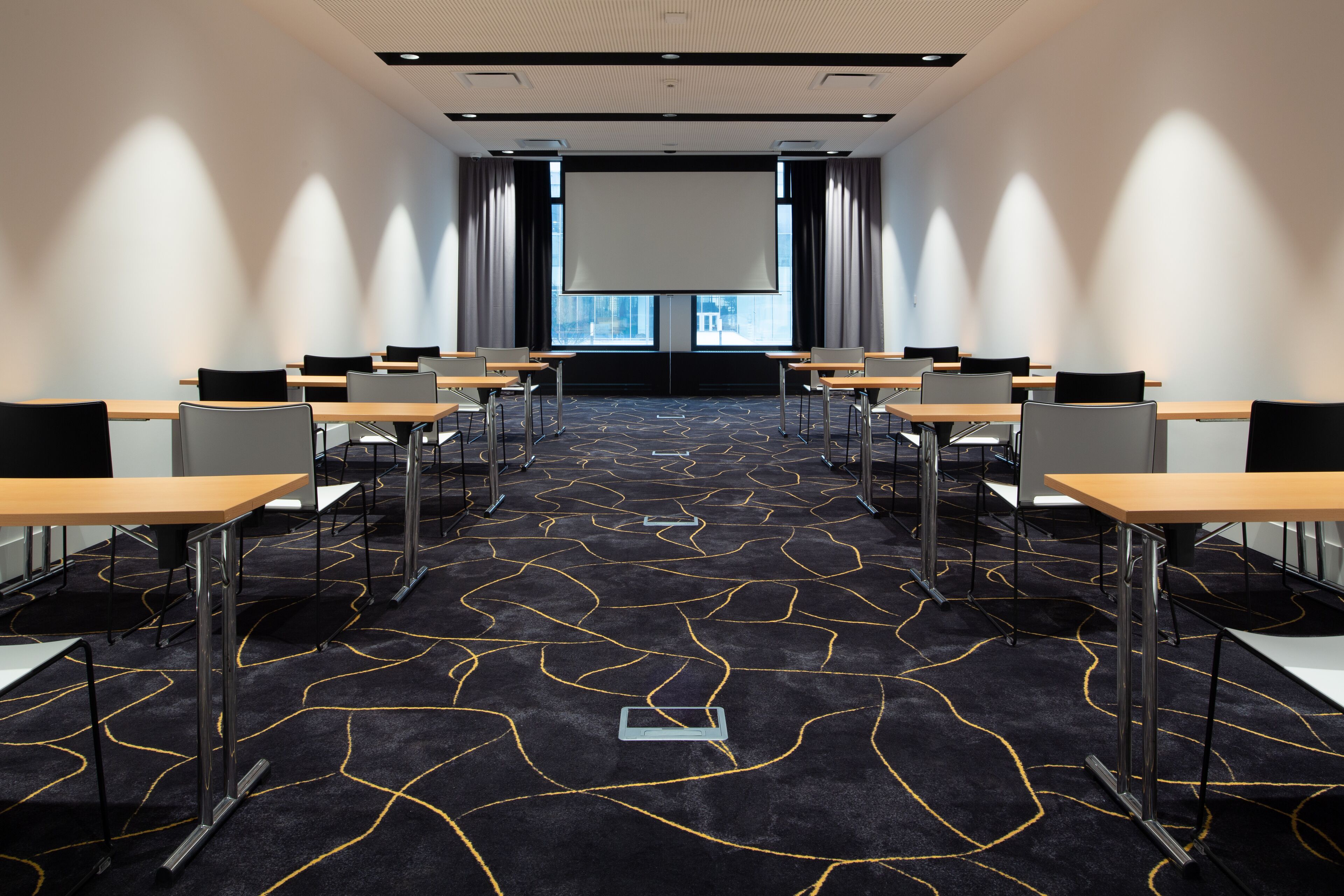 Un salón de conferencias con una pantalla grande, varias mesas y sillas dispuestas para presentaciones.