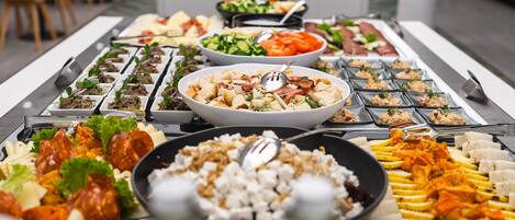 Un bufé con diversos platos, entre ellos ensaladas, carnes y quesos.