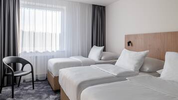 A hotel room with two beds, a chair, and a large window with sheer curtains.