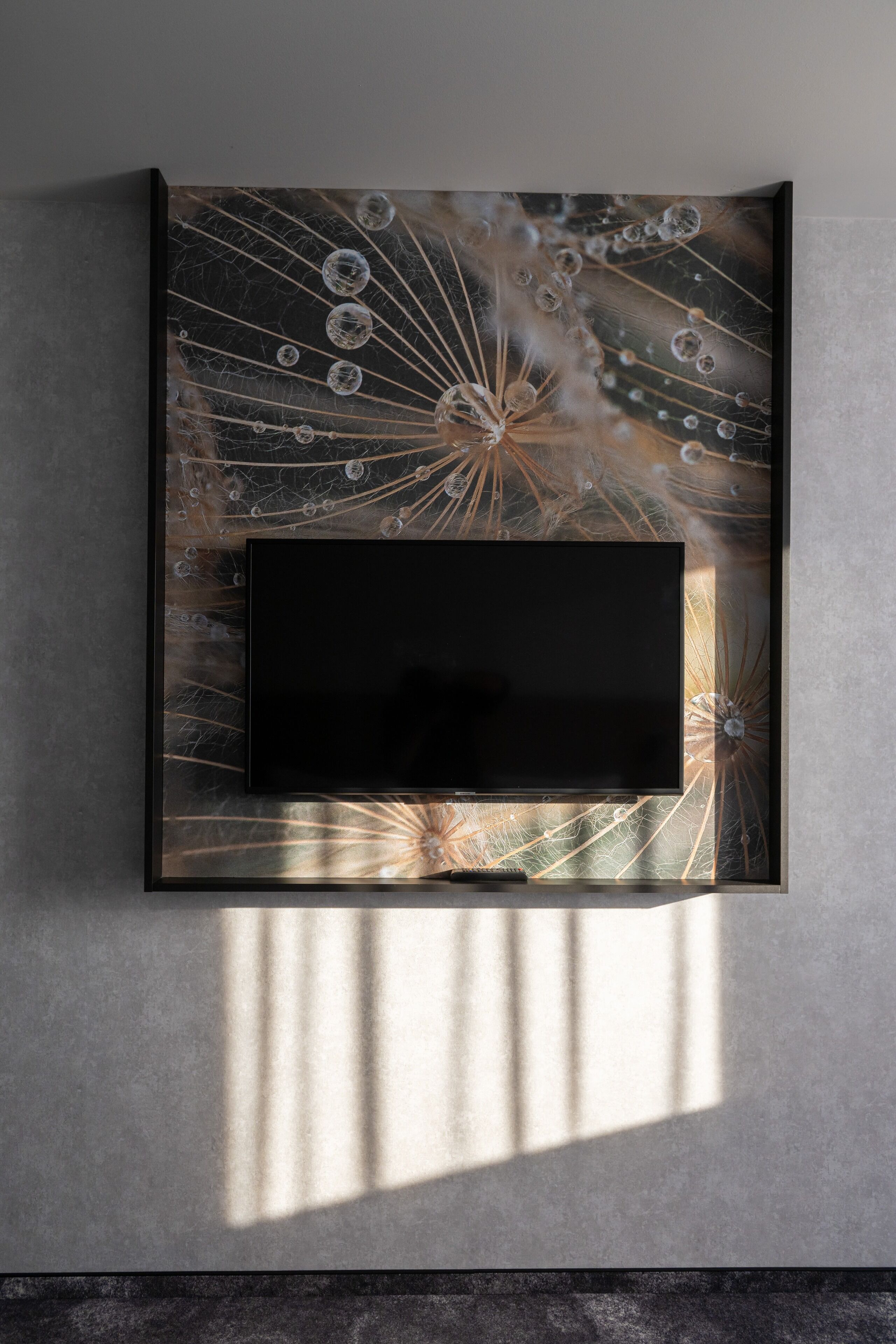A modern wall-mounted TV with a decorative glass panel featuring a dandelion design.