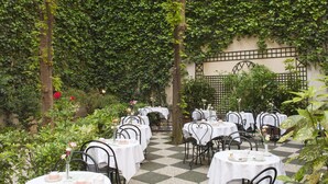 Un área de comedor al aire libre con mesas y sillas, rodeada de follaje y un suelo a cuadros.