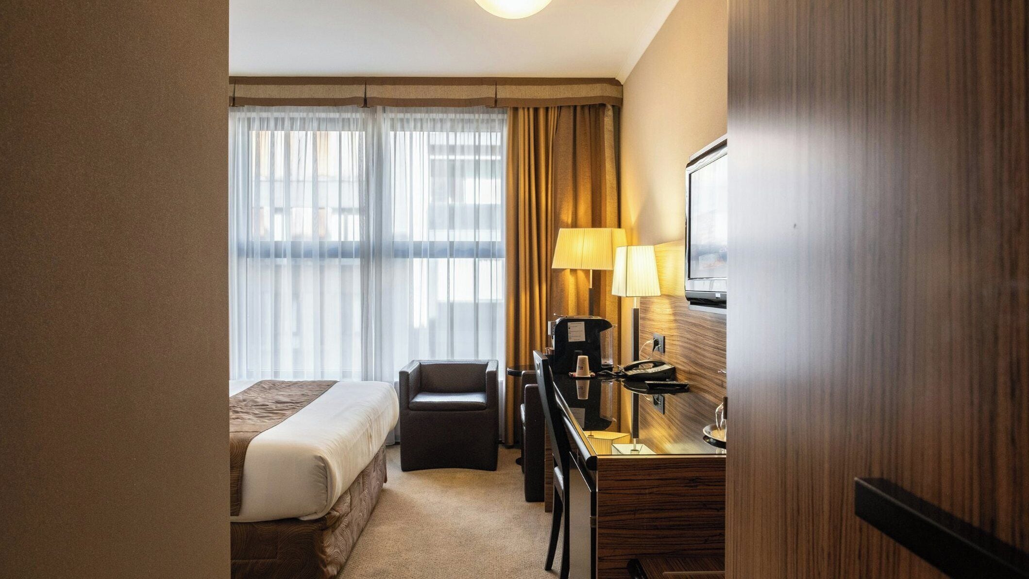 Una habitación de hotel con cama, escritorio con lámpara, silla y televisor.