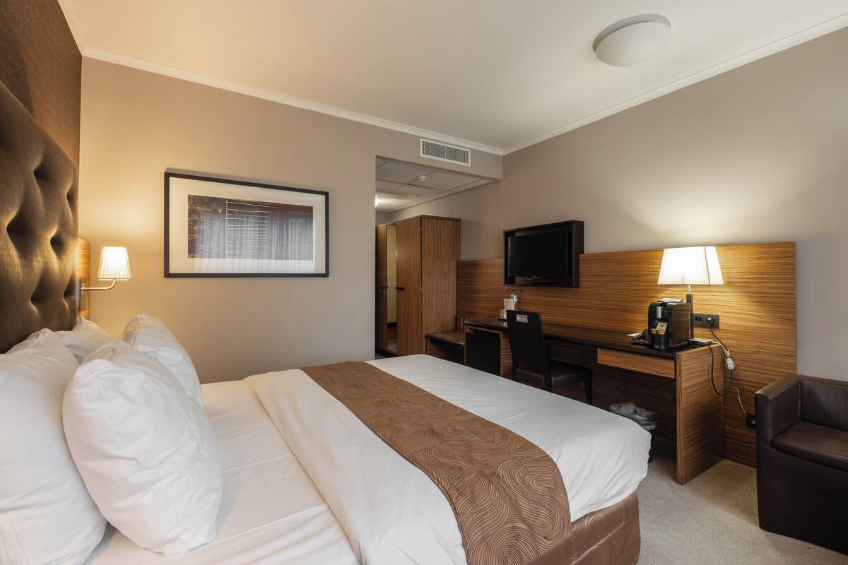A hotel room with a large bed, a desk, a chair, a television, and a lamp.