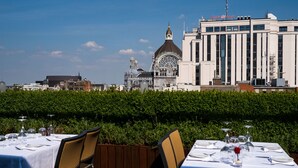 A restaurant with tables set for dining, a view of a historic building with a dome, and a clear blue sky. - Hyllit Hotel (Antwerp)