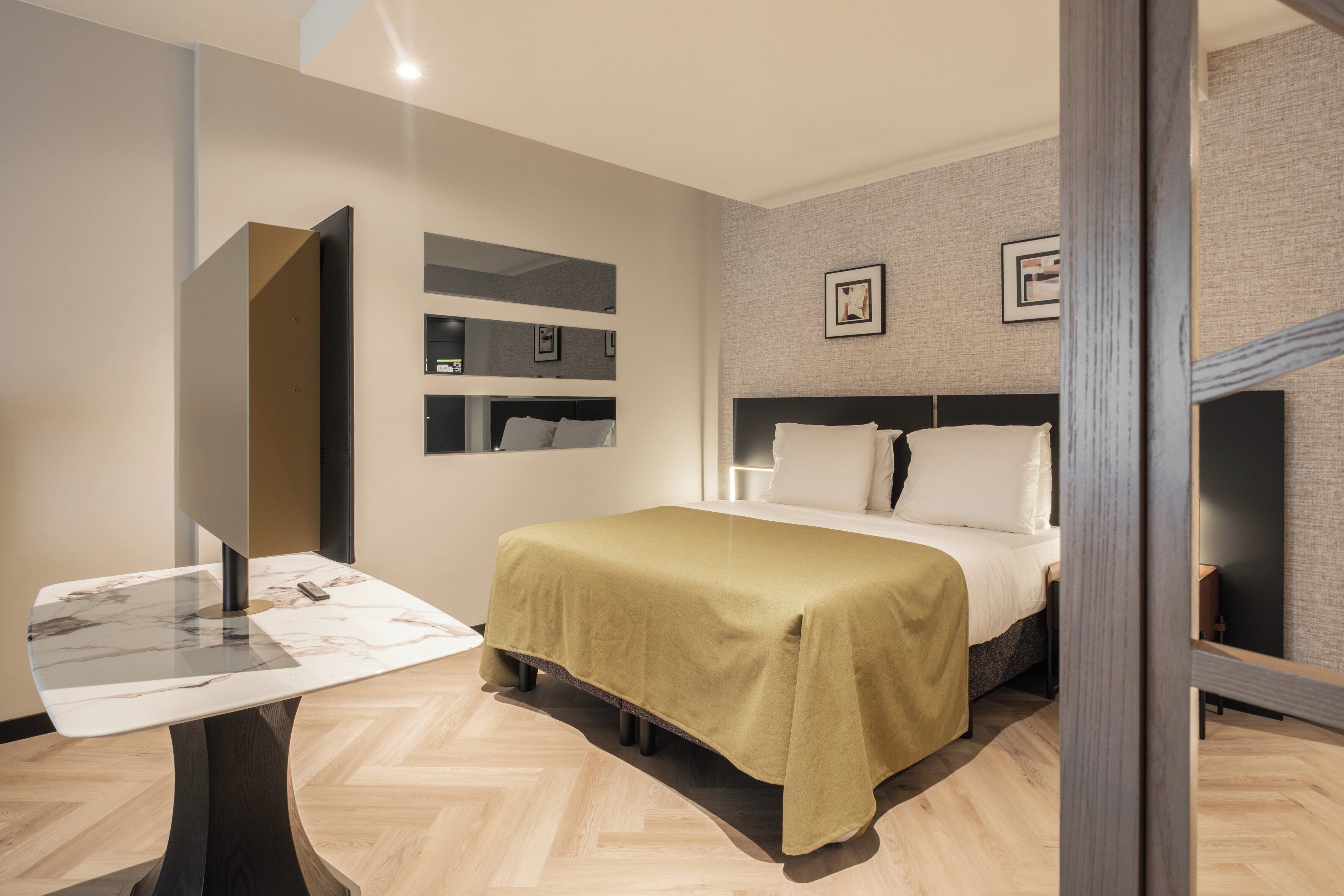 Een moderne hotelkamer met een bed, een bureau met een computer en een spiegel.