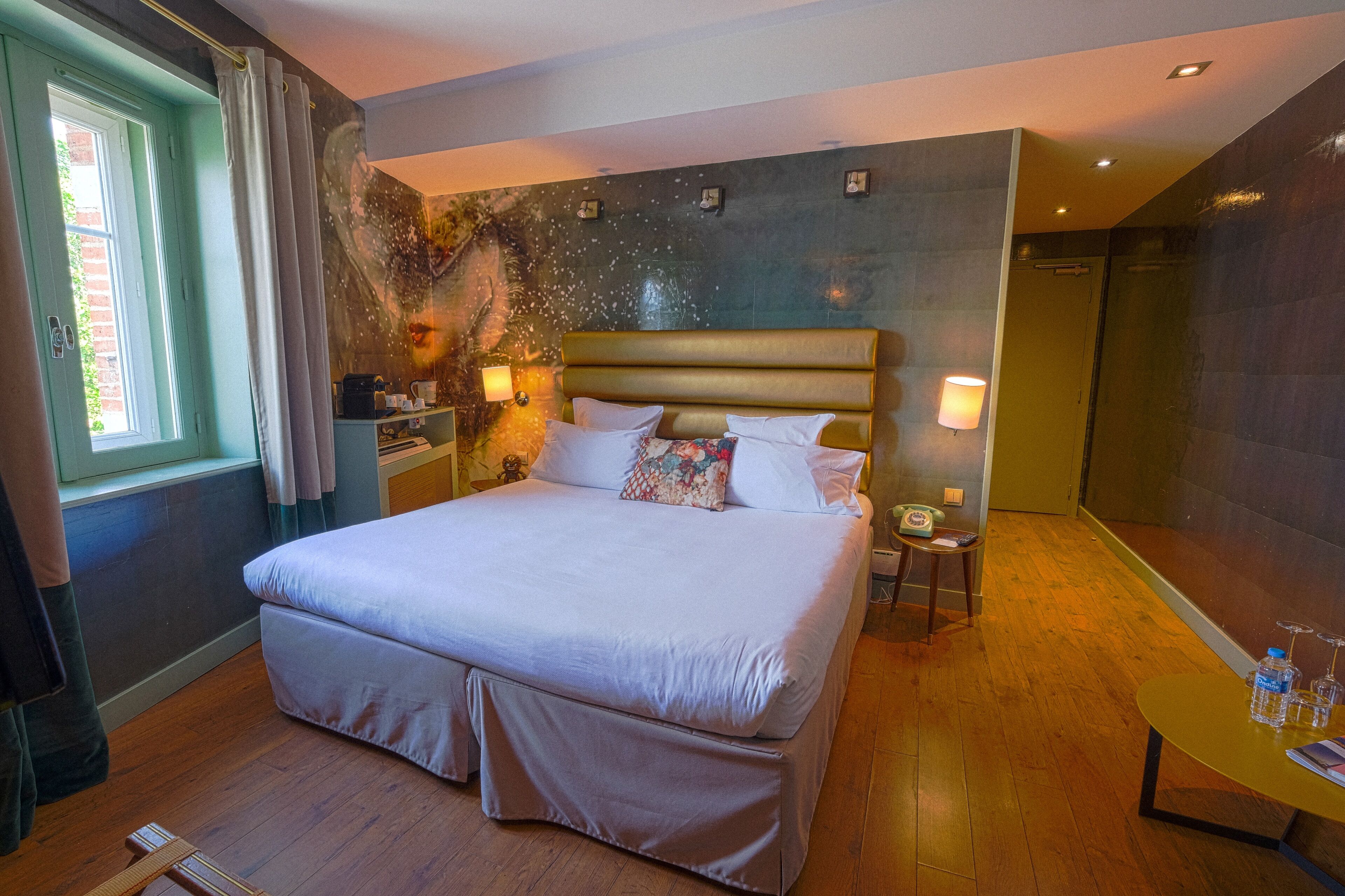 A spacious bedroom with a large bed, bedside tables, a nightstand, a window with curtains, and a wooden floor.