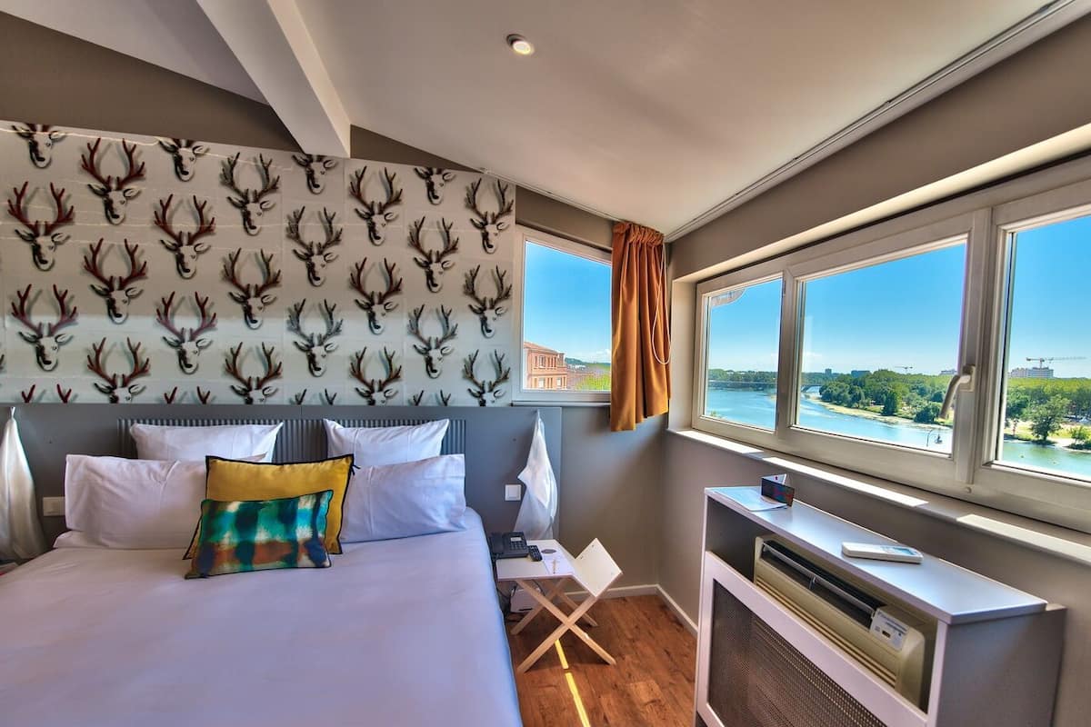 Habitación de hotel con cama, escritorio y vistas a un río y al paisaje urbano.