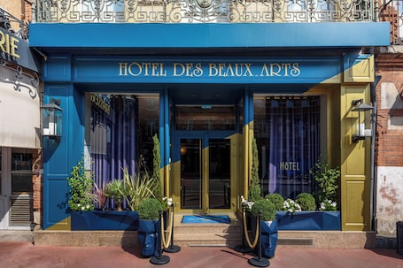 The exterior of HOTEL DES BEAUX ARTS with a blue facade, large glass windows, and a prominent entrance.