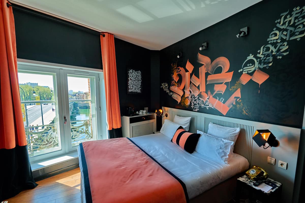 Un dormitorio moderno con una cama grande, vista a la ciudad a través de una ventana y una pared decorada con arte abstracto.