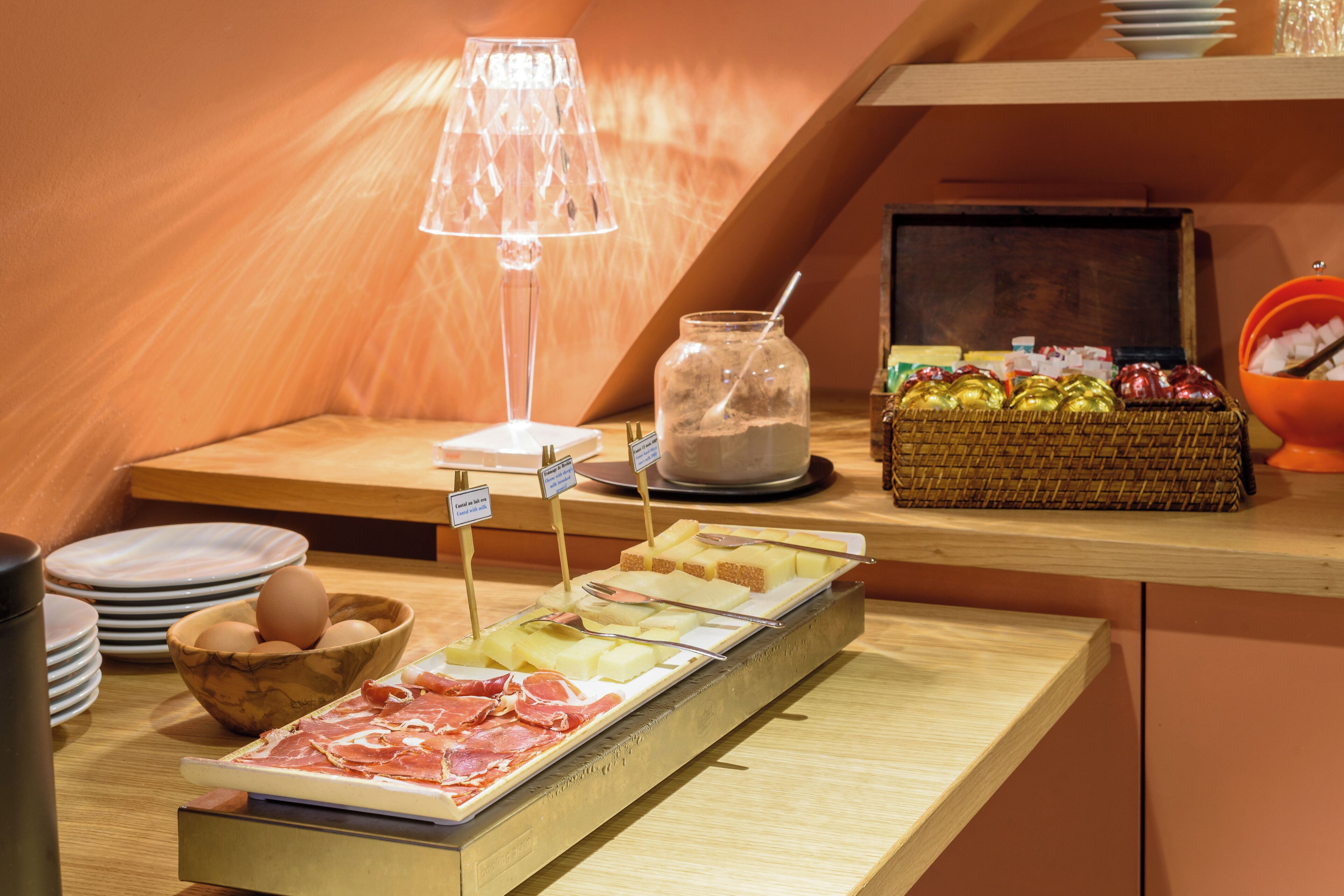 A breakfast buffet with various food items, a lamp, and a basket of fruits.