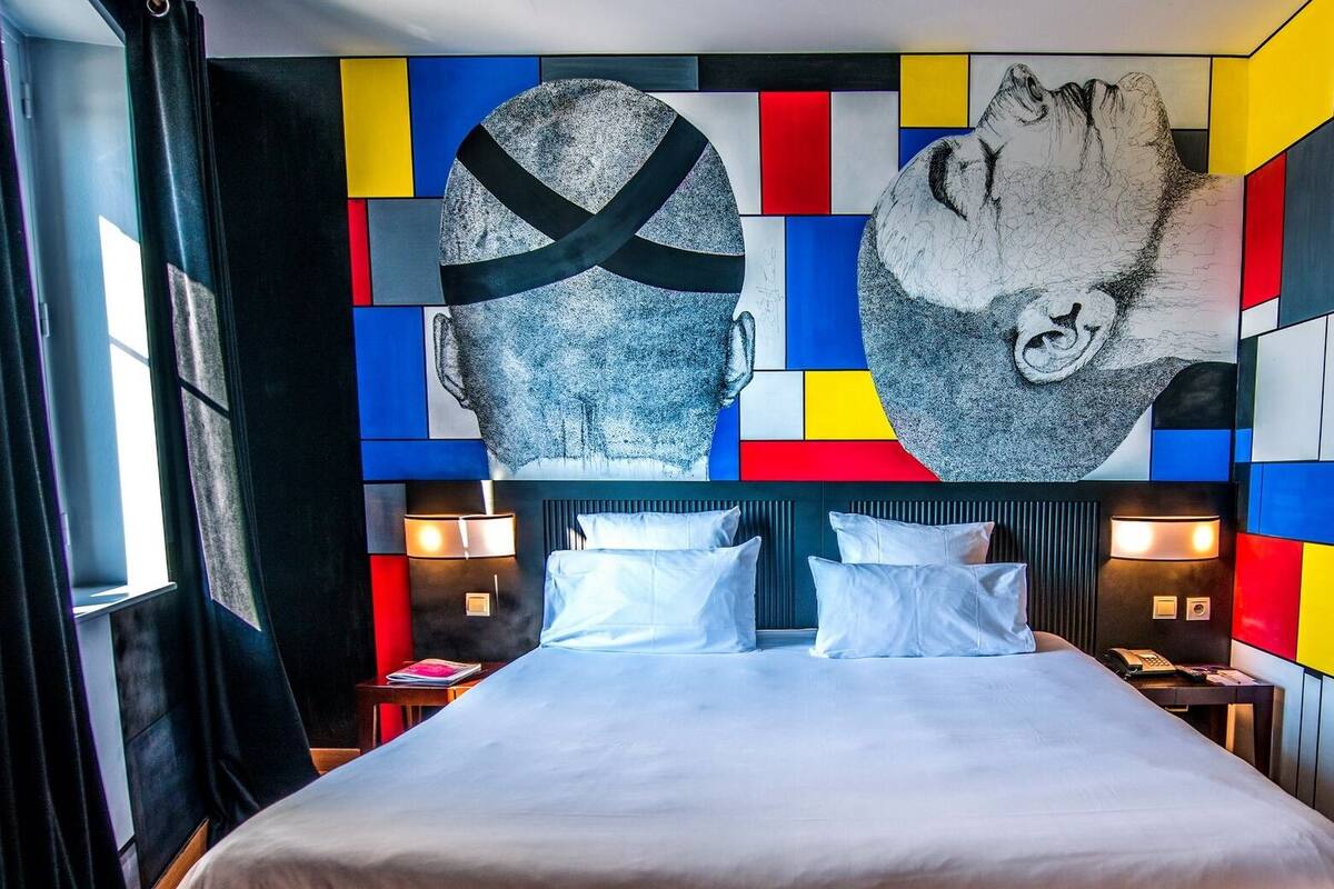 Una habitación de hotel moderna con un cuadro abstracto grande en la pared, una cama bien hecha y una mesita de noche con una lámpara.