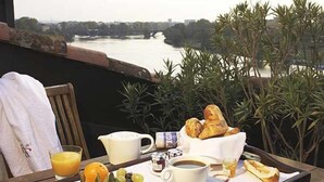 A breakfast tray with croissants, coffee, orange juice, and grapes on a balcony overlooking a river.