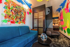 Experience a vibrant, artistic space with a comfortable sofa, glass table, and a balcony with a sliding glass door.