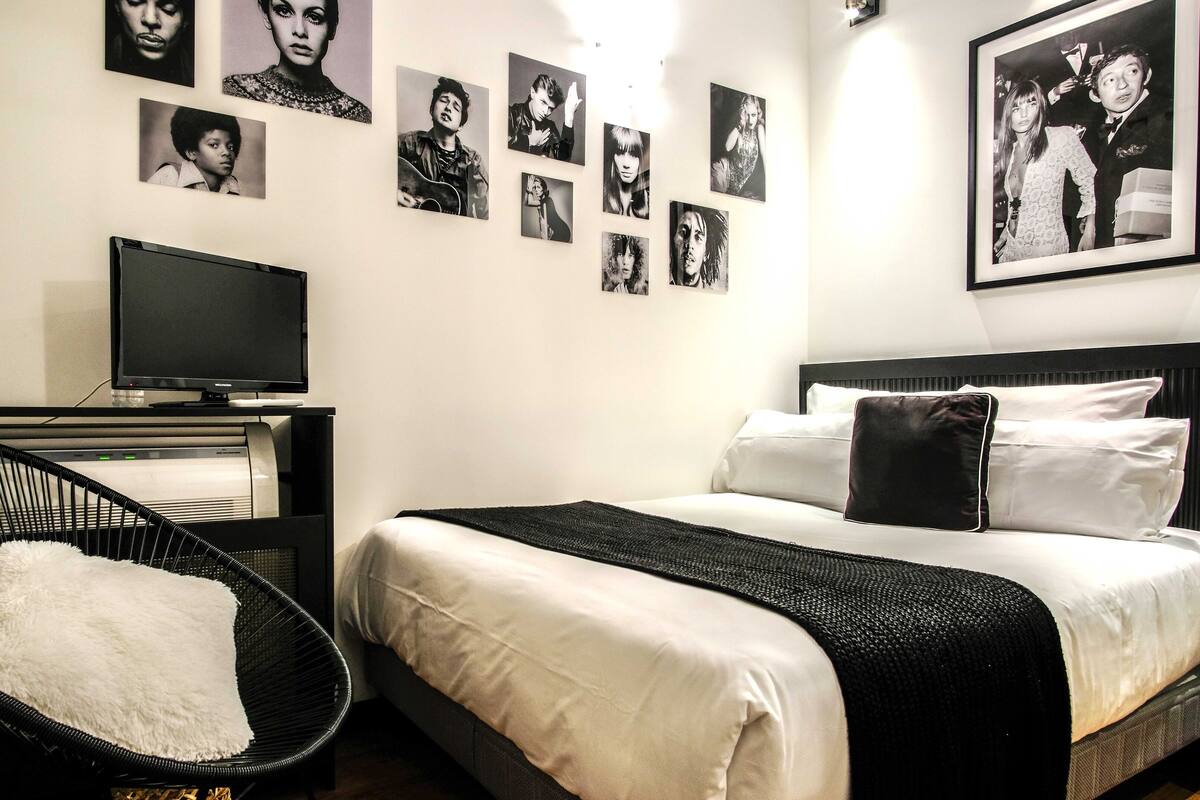 Habitación de hotel con cama, televisión, una silla negra y una pared decorada con fotografías blanco y negro.