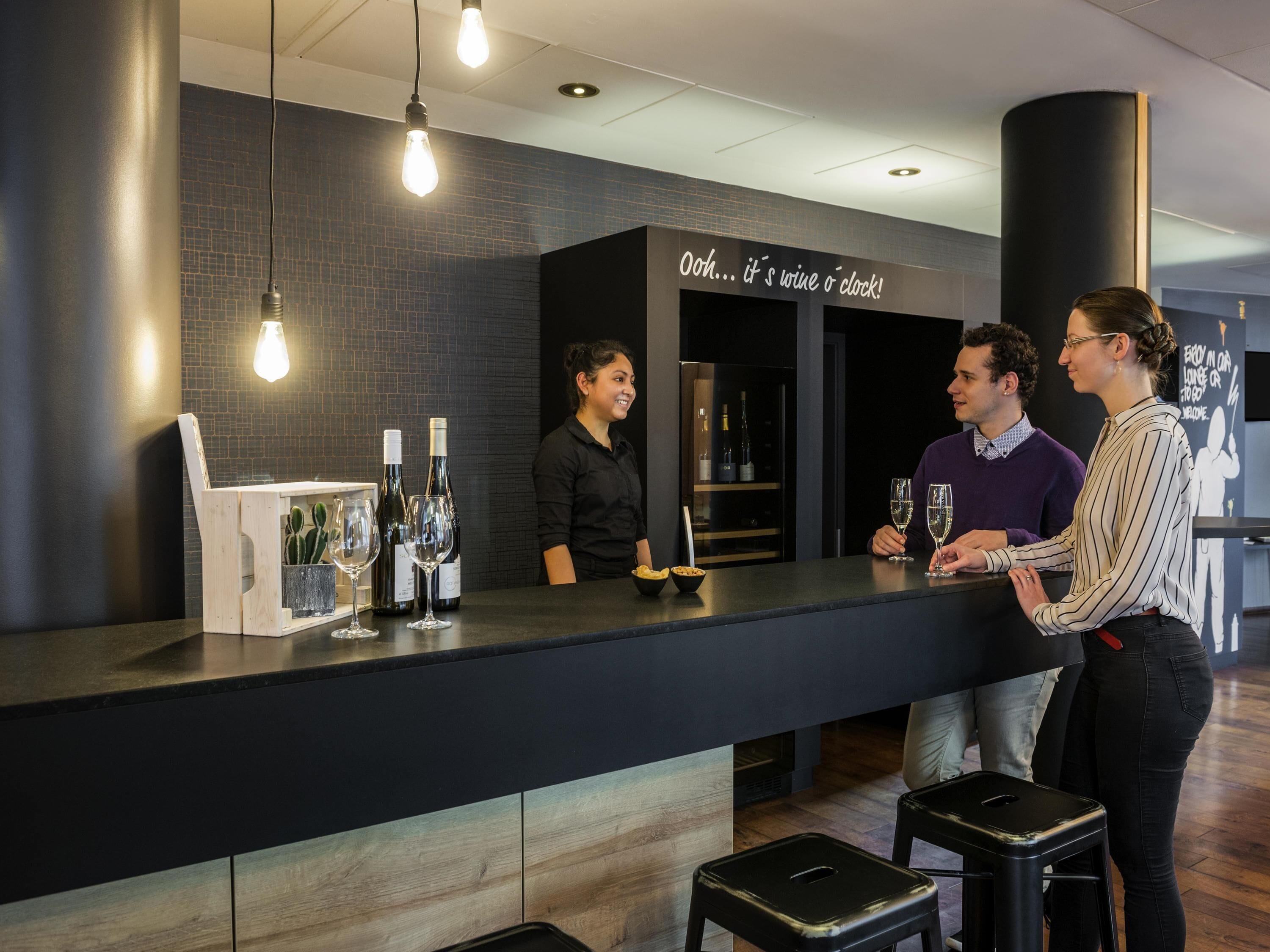 Eine Bar mit einer Theke, Weinflaschen, Gläsern und Barhocker.
