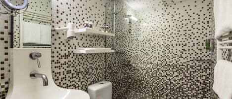A bathroom with a white sink, toilet, and shower area. There are shelves above the sink and a mirror with a ring light.