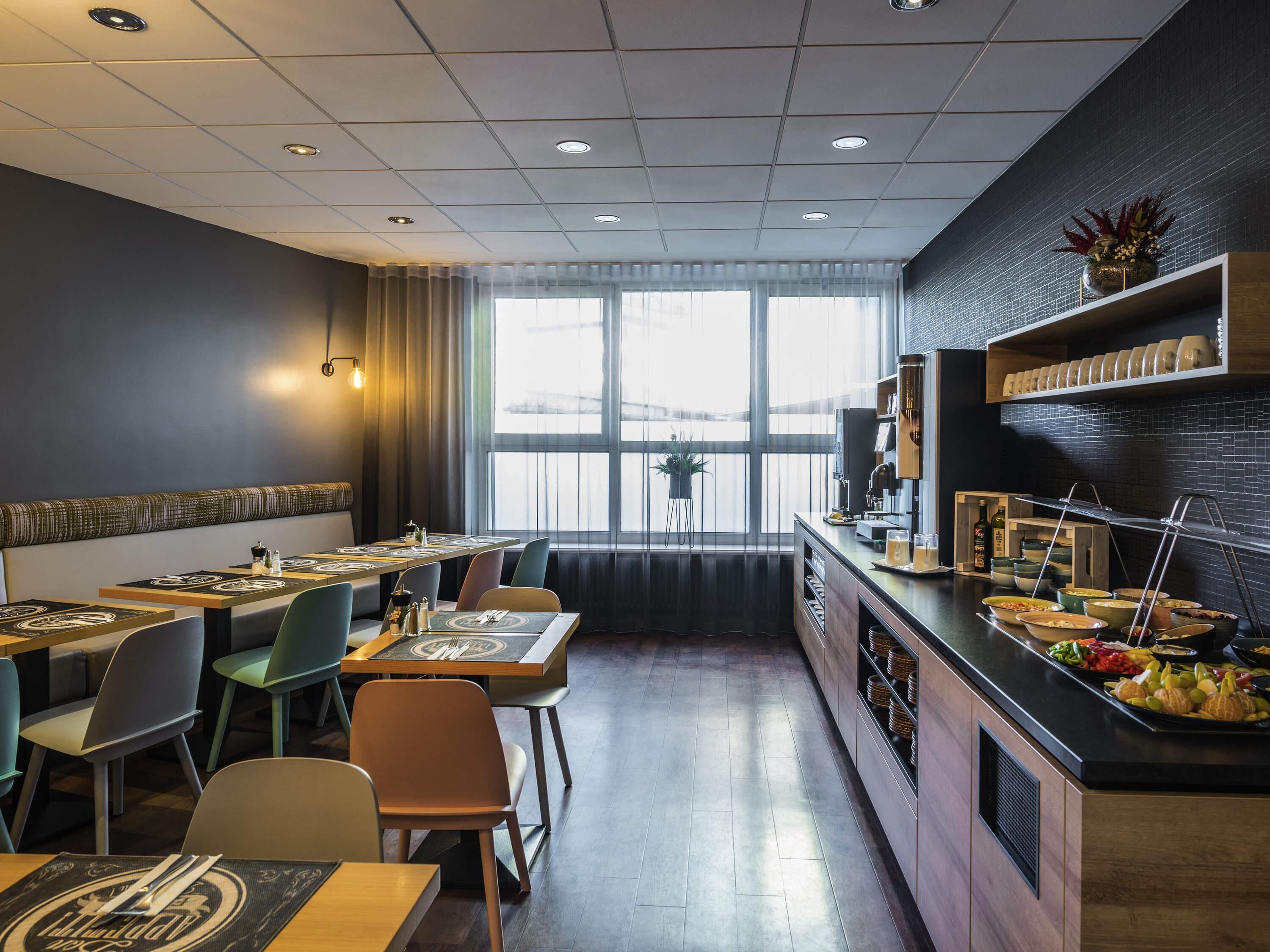 A restaurant with a long counter, multiple seating areas, and a view through large windows.