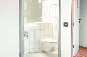 Un baño con lavamanos, inodoro y zona de ducha blanca.