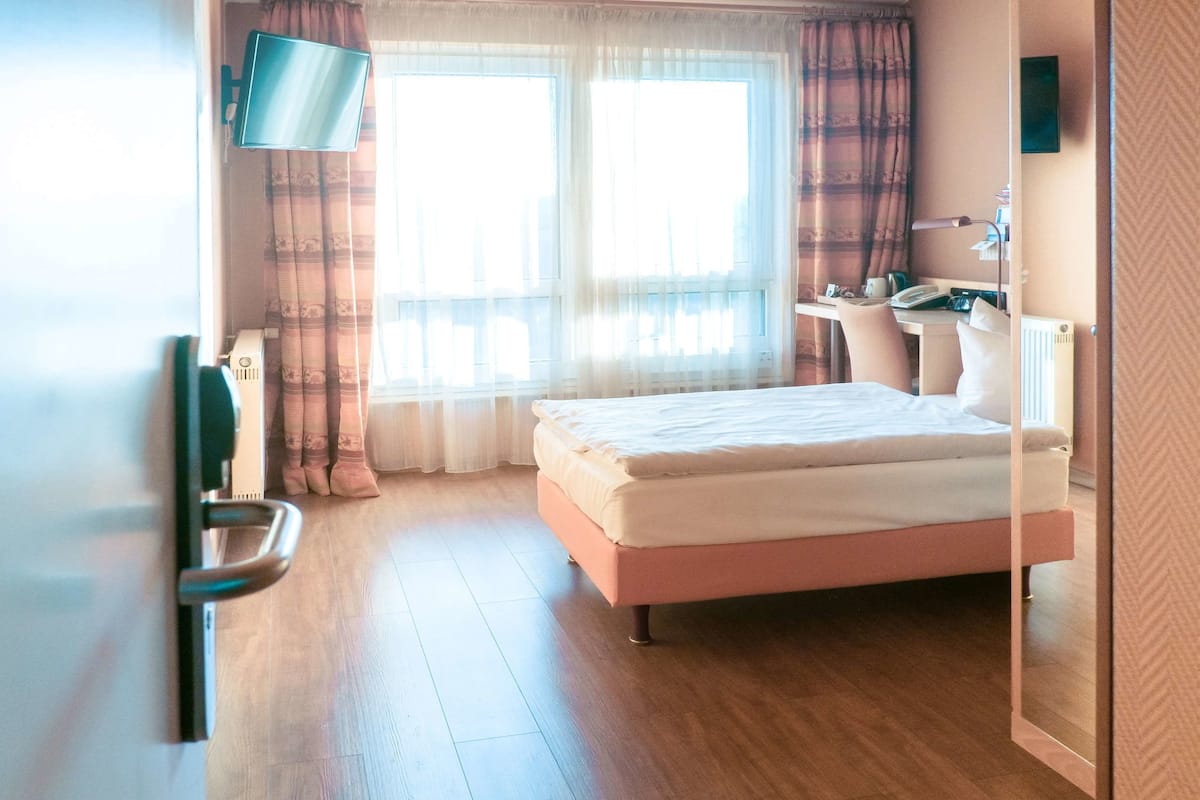 A hotel room with a bed, a desk, a chair, a TV, and a window with curtains.