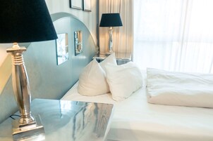 Habitación de hotel con una cama, dos mesitas de noche, una lámpara, un espejo y una ventana con cortinas.