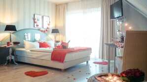 Ein ordentlich eingerichtetes Schlafzimmer mit Bett, Nachttischen, einem Fernseher und einem Fenster mit Vorhängen.
