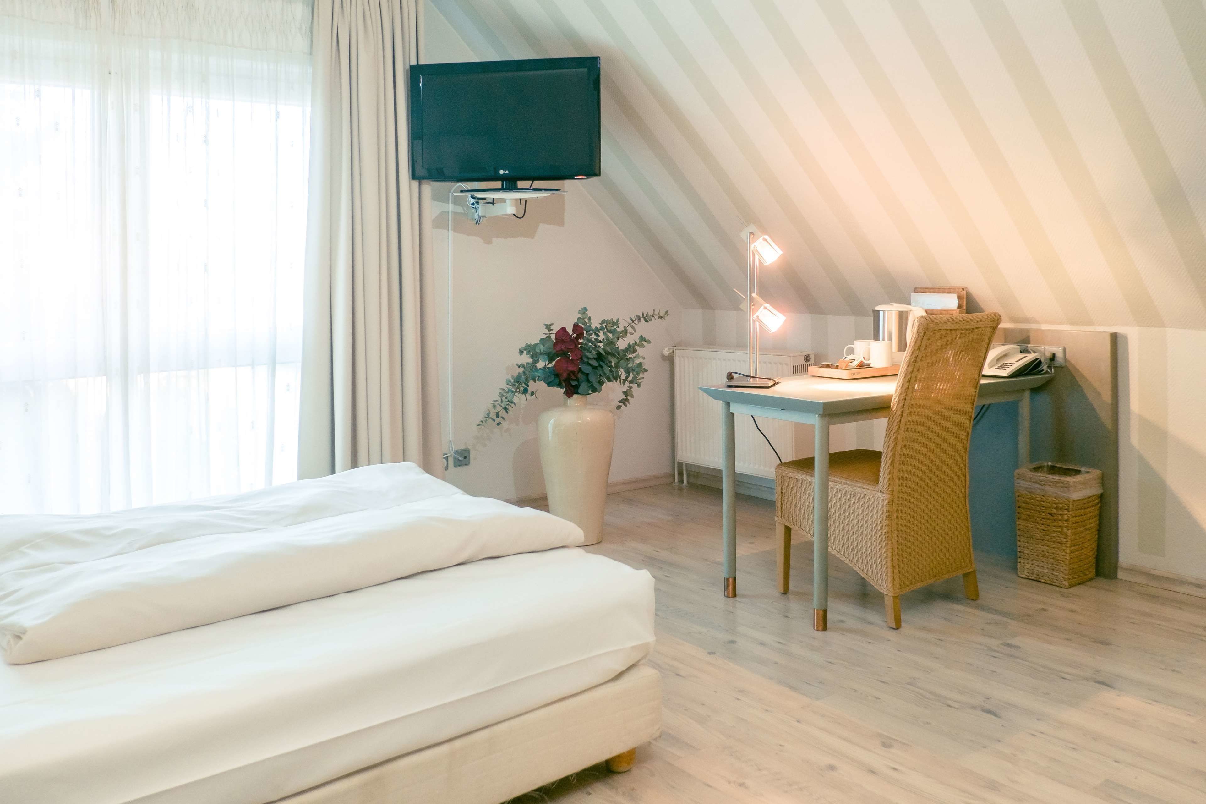 A hotel room with a bed, a desk with a chair, a television, and a vase with flowers.