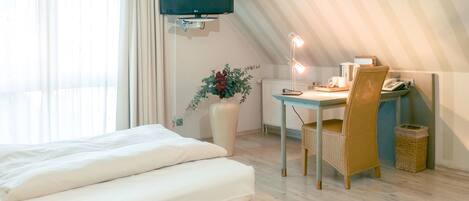 A hotel room with a bed, a desk with a chair, a television, and a vase with flowers.