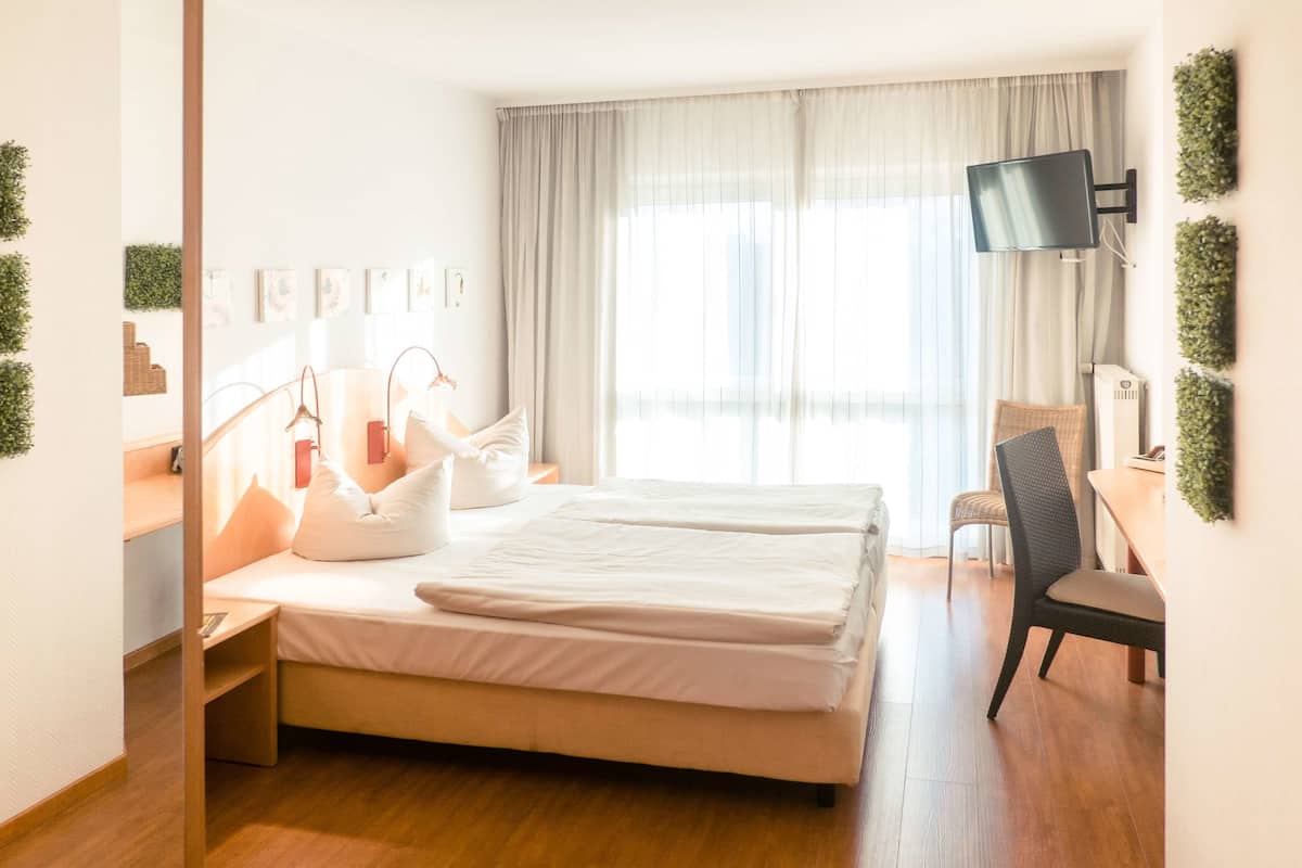 A hotel room with a bed, bedside table, lamp, chair, TV, and curtains.