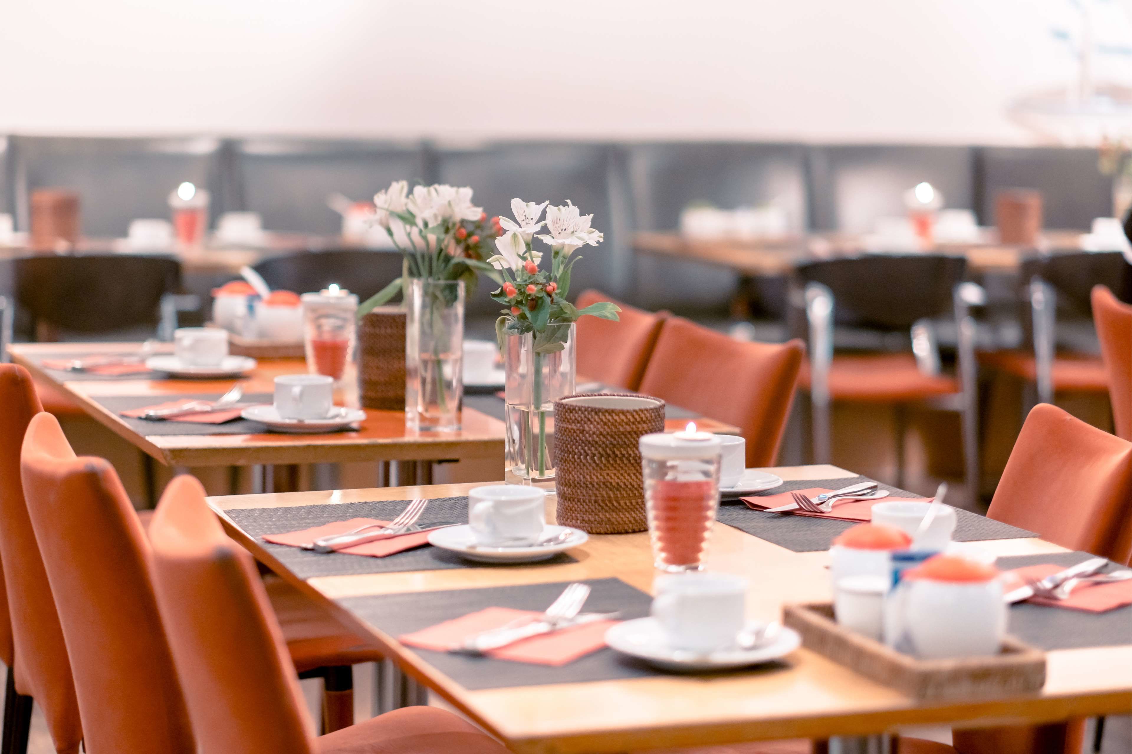 A dining area with tables set for service, featuring clear glass vases with flowers, and a wicker basket on one table.